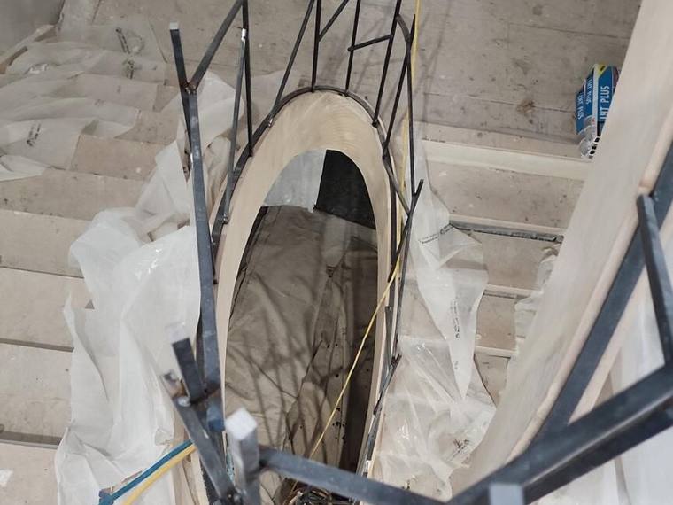 Curved iron railing being installed around an oval stair opening.