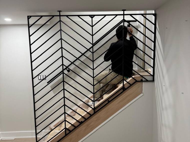 Fabricator fitting a steel railing panel to a finished stair.