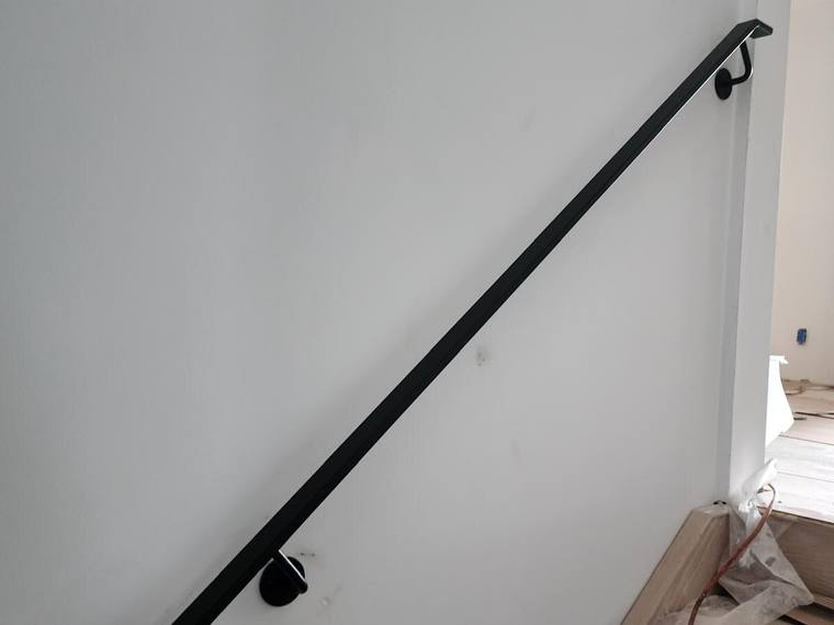 Black steel handrail mounted on a wall along a stair.