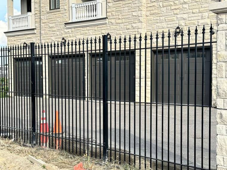 Long ornamental iron fence run broken by stone pillars.