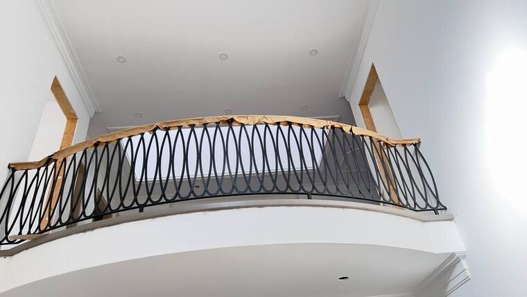 Curved iron balcony railing with a timber handrail.
