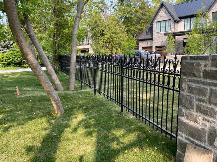 Ornamental iron fence with stone pillars along a lawn.