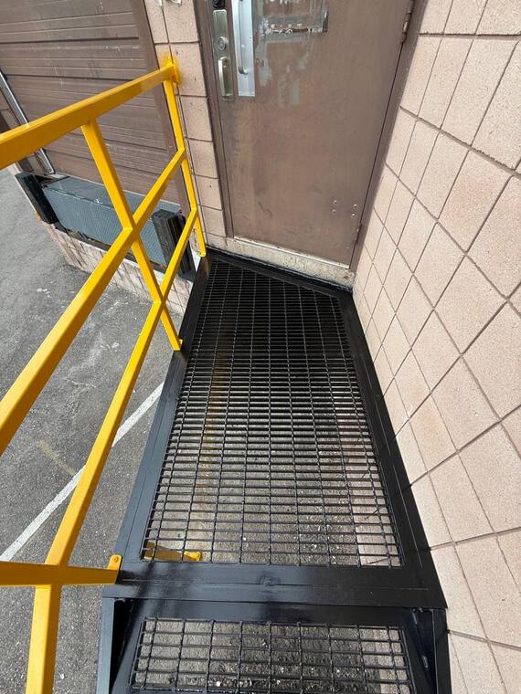 Escalera industrial instalada, con rejilla y pasamanos amarillo.